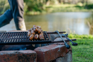 Grilling sausages over open fire at lakeside brick fire pit