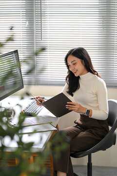 Young woman reviewing documents while working from home at a desk with desktop computer