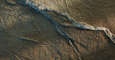 Close-up of cracked sandstone with layered white mineral vein and warm light