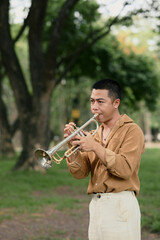 Male musician focused on playing a silver trumpet in a peaceful garden