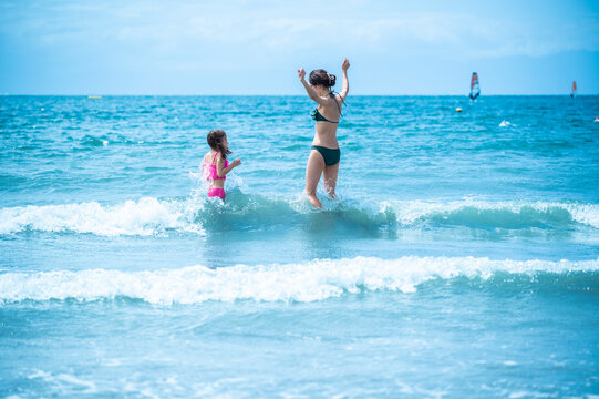 Joyful mother and daughter jumping in ocean waves at Zushi beach on a sunny summer day