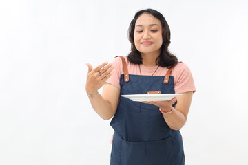 Portrait of asian woman in apron presenting something on her empty plate and smell the delicious...