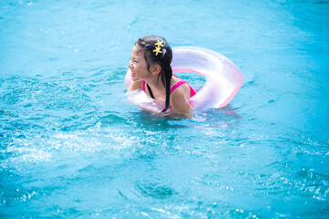 A smiling Japanese girl floats happily in turquoise sea water with a transparent pink inflatable...