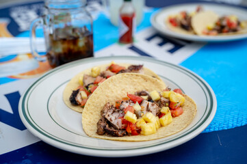 Title: Close-up of grilled pineapple and pork tacos served with tomato salsa on a white plate at a...