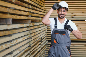 Woodworker wearing hardhat and overalls adjusting gloves in lumber warehouse