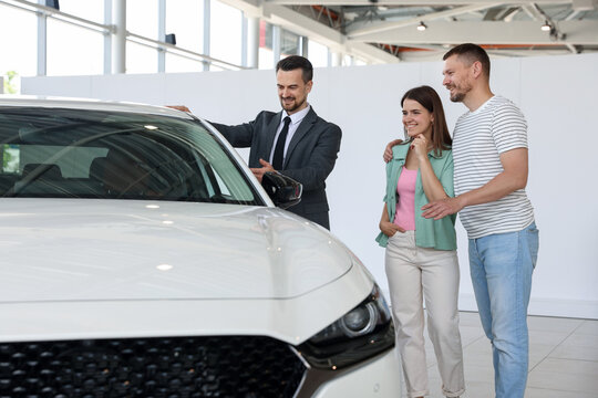 Salesman showing new car to happy family in salon