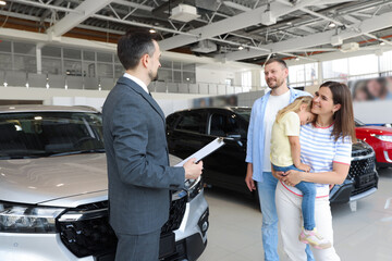Salesman with clipboard working with happy family in car salon