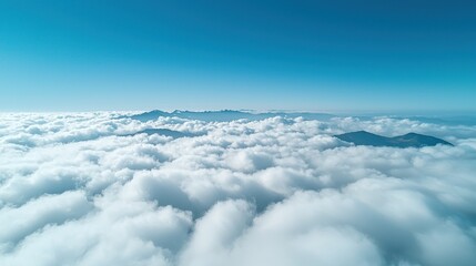 Naklejka premium High-altitude view of a vast expanse of white clouds, with mountain ranges visible through and beyond them. A clear, vibrant blue sky fills the upper portion of the image
