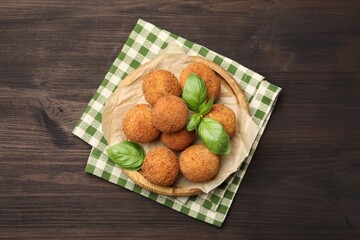 Delicious fried croquette balls with basil on wooden table, top view