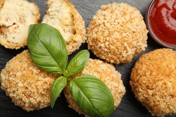 Delicious fried croquette balls with basil and ketchup on grey textured table, flat lay