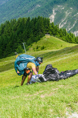 Paraglider Pilot Preparing Wing for Flight on Sunny Green Slope in Mountain Area. High quality photo