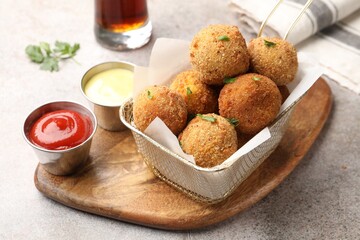 Delicious fried croquette balls with parsley and sauces on grey textured table, closeup