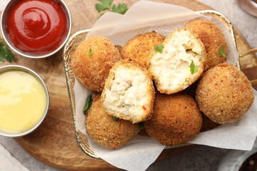 Delicious fried croquette balls with parsley and sauces on grey textured table, flat lay