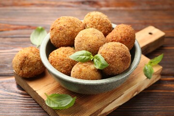 Delicious fried croquette balls with basil in bowl on wooden table, closeup