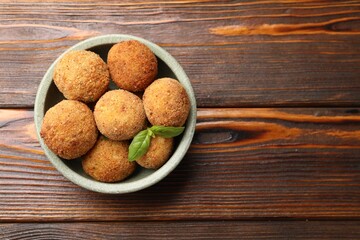 Delicious fried croquette balls with basil in bowl on wooden table, top view. Space for text