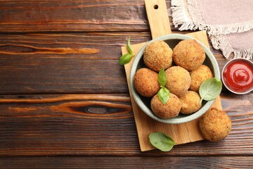 Delicious fried croquette balls with basil in bowl and ketchup on wooden table, flat lay. Space for...