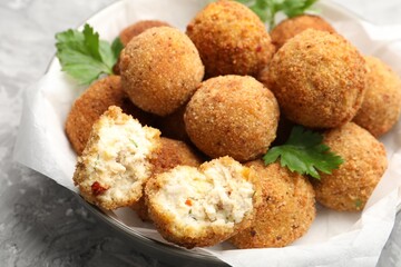 Delicious fried croquette balls with parsley in bowl on grey textured table, closeup