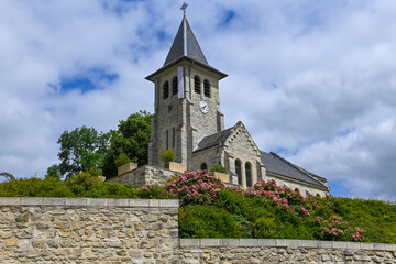 Photo of the church on a hill in the French village of Neuville sur Aillete, against a summery blue sky with white clouds.