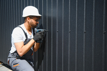 Construction worker installing metal siding on building using cordless drill