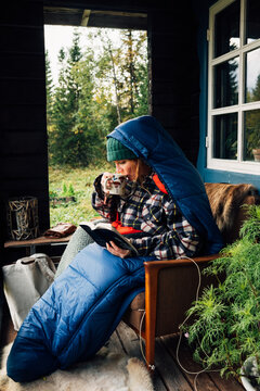 Woman relaxing in sleeping bag, reading and drinking tea on cabi