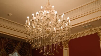 Grand crystal chandelier glowing warmly in richly decorated room with red walls, gold trim, and ornate ceiling and curtain details, radiating classic luxury and elegance - Powered by Adobe