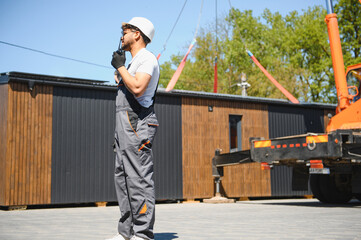 Construction worker supervising lifting of modular house onto truck