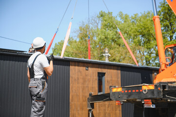 Construction worker supervising lifting of modular house onto truck