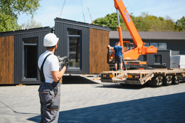 Construction worker supervising loading of modular house onto truck