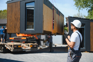 Construction worker supervising loading of modular house onto truck