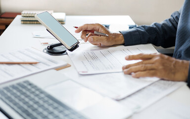 asian businessman working on desk using smart phone checking business documents in office