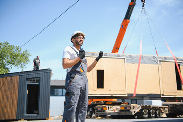 Construction worker supervising lifting of modular house onto truck