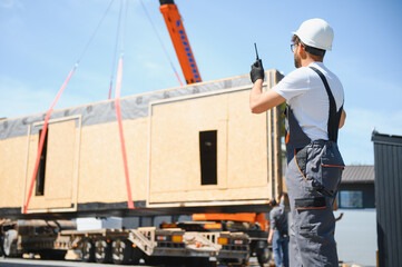 Construction worker supervising loading of modular house onto truck