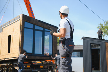 Construction worker supervising loading of modular house onto truck
