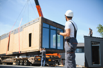 Construction worker supervising loading of modular house onto truck