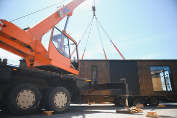 Crane lifting prefabricated modular house onto truck for transportation