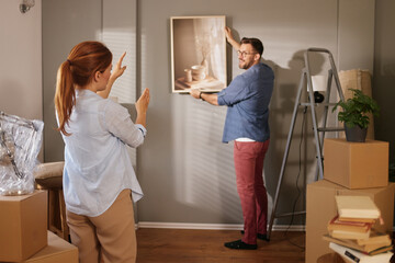 A couple is in the process of organizing their new living space. One person holds a piece of...