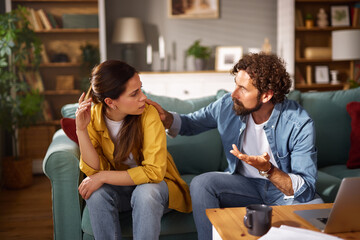 A man comforts a woman as they sit on a couch in a cozy living room, engaged in a serious...