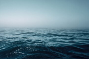 Fototapeta premium Calm, dark-blue ocean surface stretches to a hazy, light-blue horizon under a clear sky. Gentle waves ripple