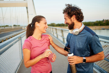 Two individuals engage in a friendly conversation while jogging on a bridge, showcasing their...