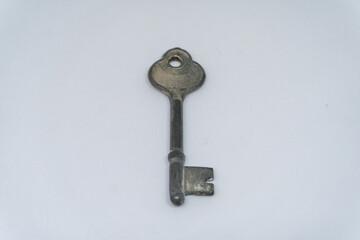 A single, tarnished, antique key lies centered on a plain white surface, casting a subtle shadow.