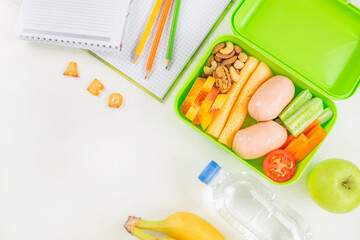 Healthy school lunch in a green lunchbox with vegetables, cheese, sausages, nuts, fruit, and a...