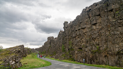 Unidentified tourists walking along in Thingvellir National Park, where the Eurasian and North American tectonic plates visibly separate through a rocky stream gorge.