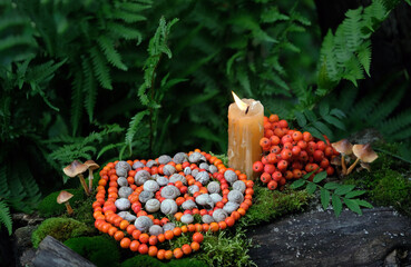 Candle and spiral made of snail shells and rowan berries in forest. Witchcraft, protective rowanberry practice. Wiccan spiritual esoteric ritual for Mabon holiday. nature mandala for green magic