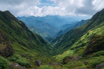 Vast mountain valley under a cloudy sky showcasing lush green slopes and distant peaks