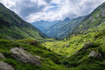 Obraz premium Vast alpine valley under dramatic clouds revealing lush green slopes and jagged peaks