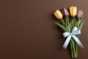 Beautiful yellow and purple tulips arranged with a blue ribbon on a dark brown background providing an elegant look
