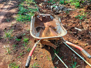Old, dirty and rusted single wheel cart on soil pile at garden. Metal construction trolley....