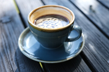 Cup of black espresso coffee on wooden table, close-up, outdoors