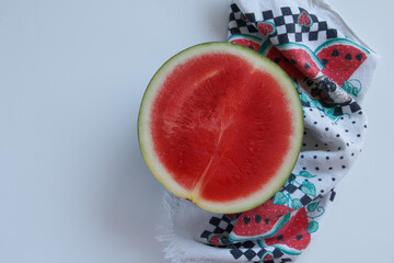 Half seedless watermelon with watermelon-patterned kitchen towel on white background