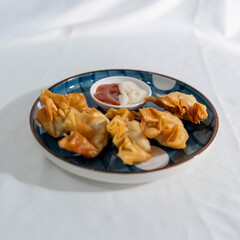 A serving of fried wontons on a blue-patterned plate with ketchup and mayonnaise, shot in natural lighting on a soft white fabric.